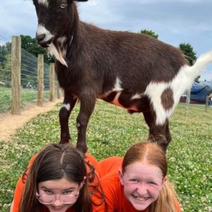 Two teenagers with goat on their backs at goat yoga
