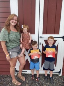 Redheaded family standing in front of a red barn on Redhead Celebration Day with two boys holding content certificates.