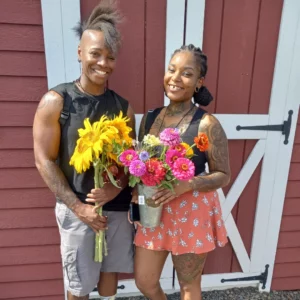 Couple holding fresh sunflowers and flowers in front of red barn
