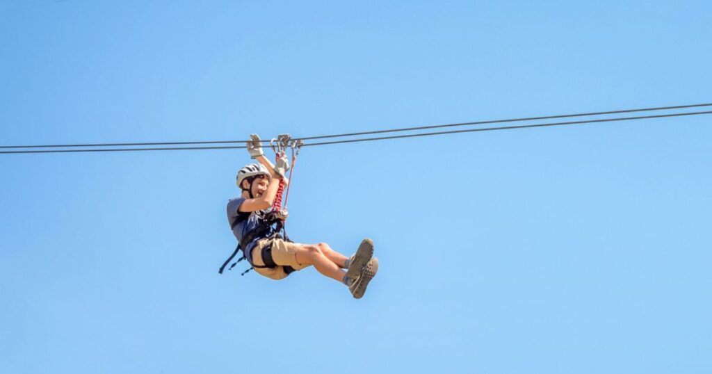 Teen on Zipline in PA wearing safety harness and helmet.