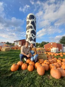 Couple posing with pumpkins in front of Hellericks Farm cow silo