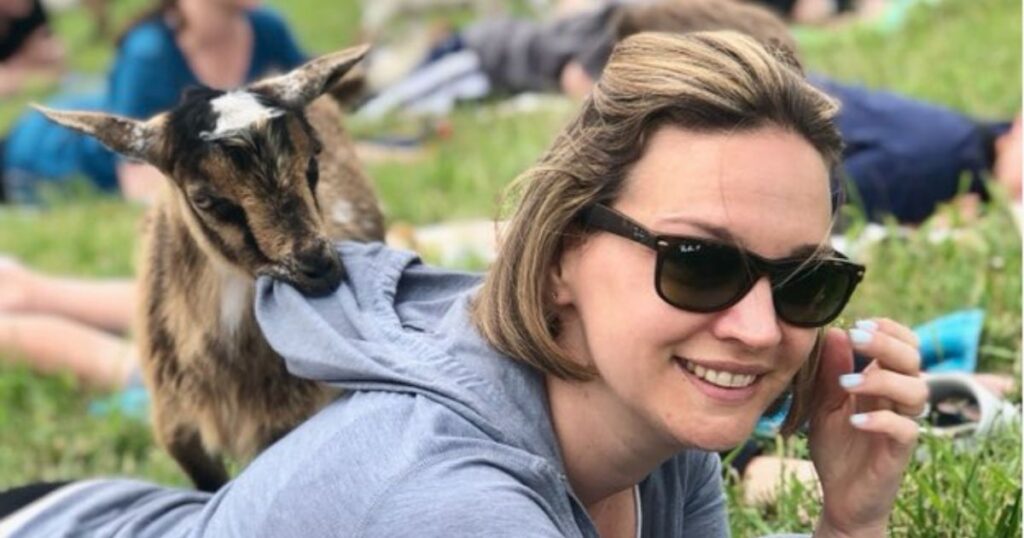 Woman in a goat yoga class wearing a grey hoodie with a young goat biting the fabric.