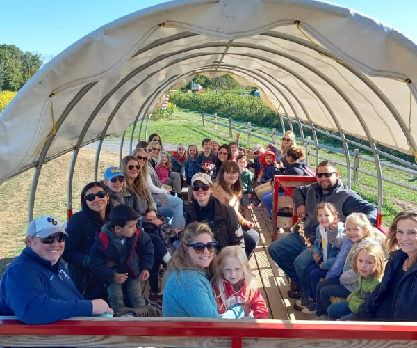 a group of families riding on a tractor wagon together on a sunny day