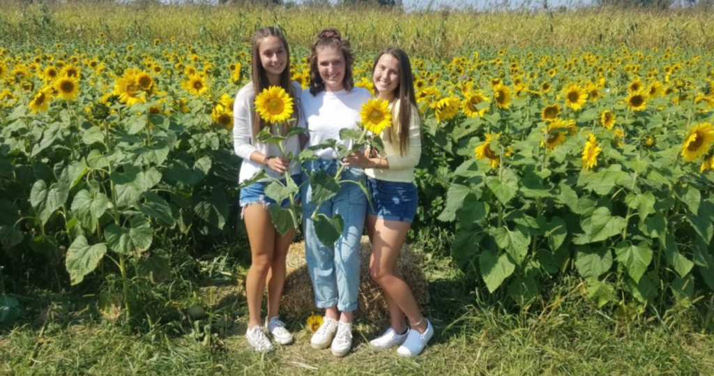 Girls posing with sunflowers in front of a sunflower field in PA